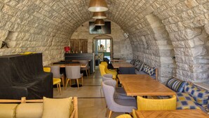 Interior de piedra con arco, mesas y sillas de madera, una zona de cocina y vistas a través del arco.