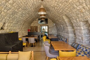 Interior de piedra con arco, mesas y sillas de madera, una zona de cocina y vistas a través del arco.