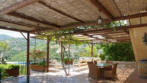 Un patio al aire libre con mobiliario de madera, una pérgola y vistas a un paisaje montañoso.