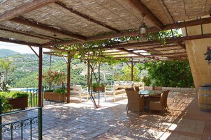 Un patio al aire libre con mobiliario de madera, una pérgola y vistas a un paisaje montañoso.