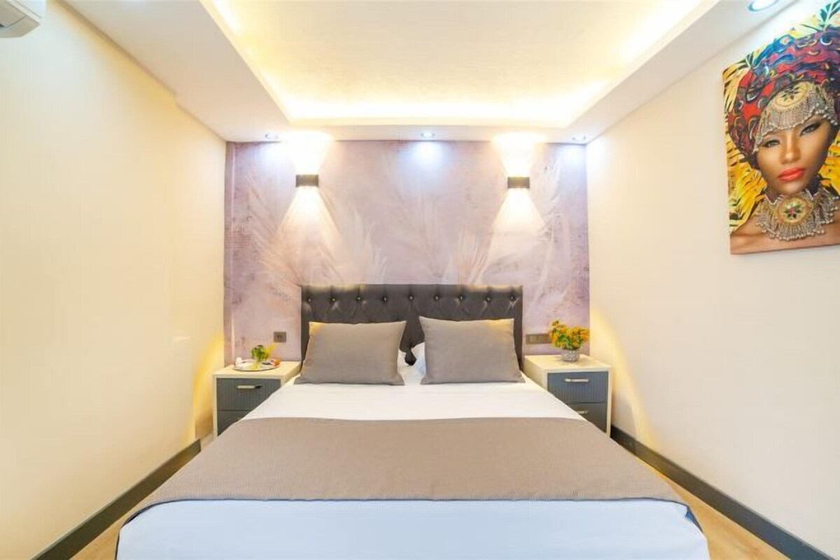 A neatly made bed with a headboard, two bedside tables, and a wall-mounted painting.