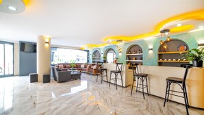 Un hall d’entrée moderne avec un sol en marbre, un espace détente avec des canapés et des fauteuils, et un comptoir d’accueil orné d’étagères remplies d’objets.