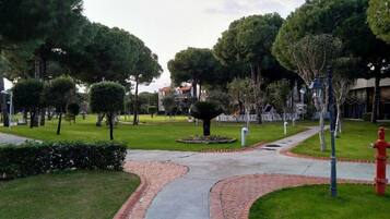 Un sendero pavimentado en un parque con árboles y un hidrante rojo.