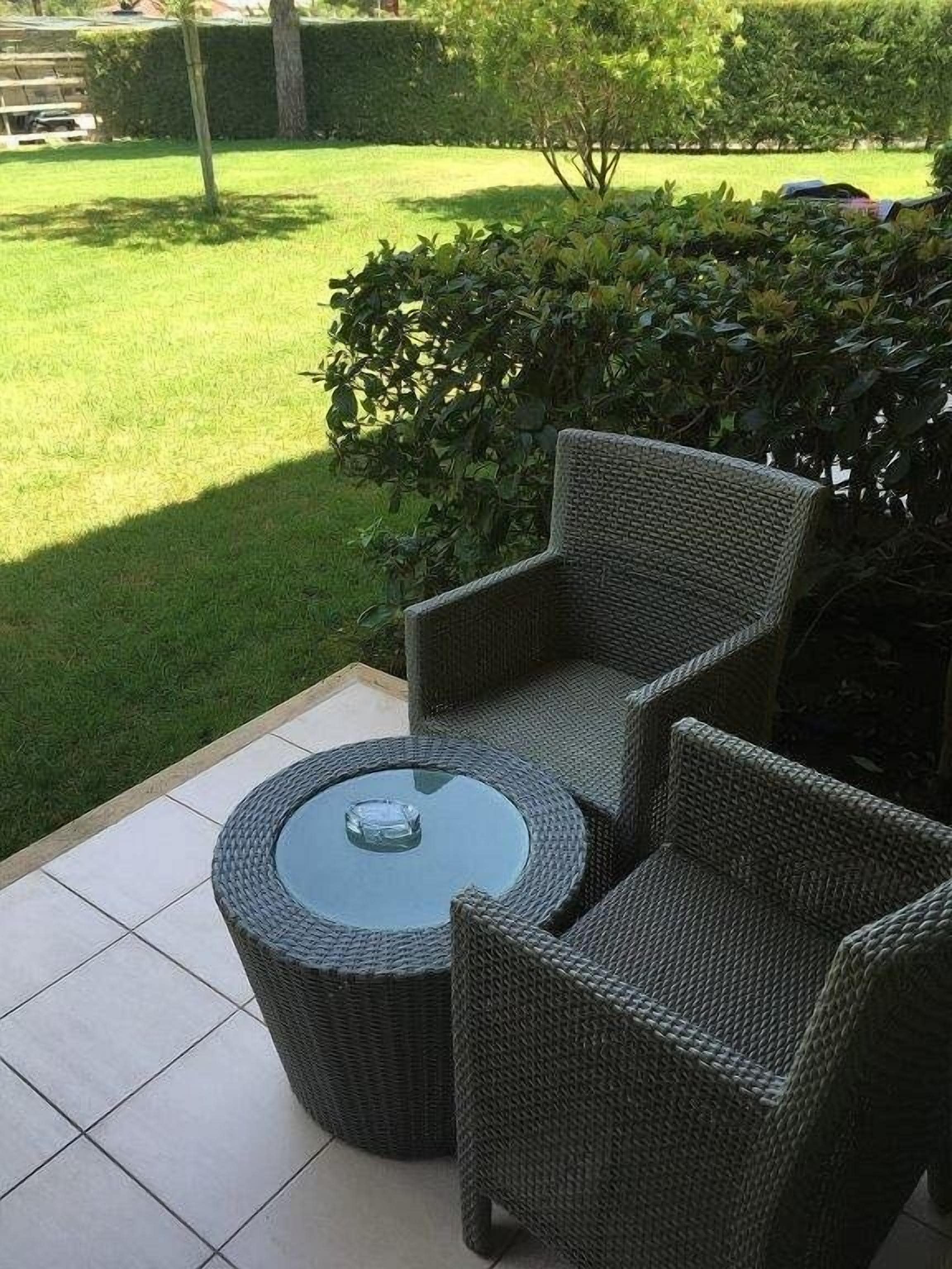 Un espacio al aire libre con mobiliario de mimbre y una mesa con superficie de vidrio.