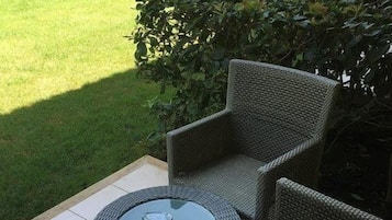Un espacio al aire libre con mobiliario de mimbre y una mesa con superficie de vidrio.