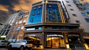 A hotel with a coffee shop and restaurant on the ground floor, featuring a modern design with large windows and a prominent sign.