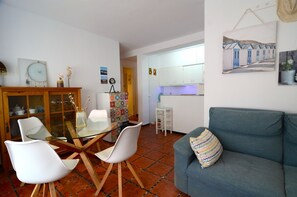 Een woonkamer met een eettafel met glazen blad, witte stoelen, een blauwe bank en een kast met glazen deuren.