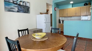 A dining area with a round wooden table, two chairs, a woven placemat, and a white refrigerator.