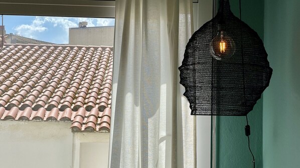 A window with a view of a tiled roof, a white curtain, and a hanging light fixture.