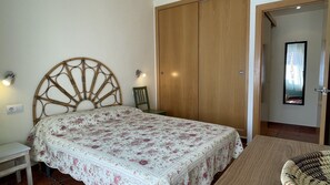 A bedroom with a bed, a wooden wardrobe, a chair, and a small table. - PUIG SUREDA 36 2-1 (L'Escala)