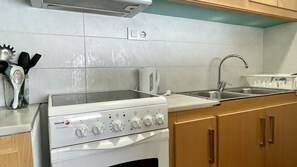 A kitchen with a stove, sink, and wooden cabinets. - PUIG SUREDA 36 2-1 (L'Escala)
