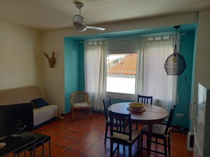 Un comedor con una mesa redonda, sillas, un ventilador de techo y una ventana con cortinas.