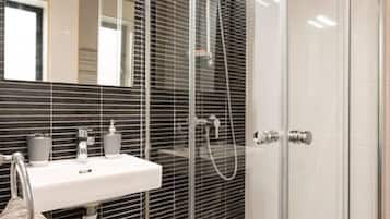 Ein modernes Badezimmer mit einer Glaskabine zur Dusche, einem weißen Waschbecken und einem Spiegel darüber.