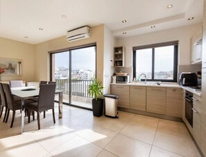 A modern apartment with a dining area, kitchen, and large windows offering city views.