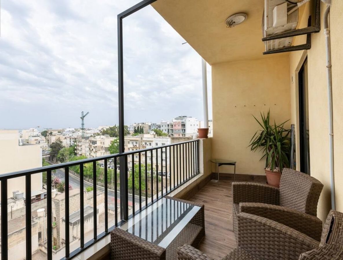 Ein Balkon mit Korbmöbeln, einem Blumentopf und Blick auf die Stadtlandschaft.