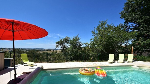 Una piscina con sillones de descanso y una sombrilla, rodeada de árboles y vistas al campo.