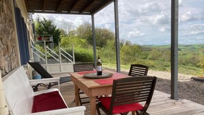 Un patio al aire libre con una mesa de madera, dos sillas y una botella de vino.