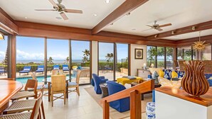 Un espacio interior amplio con vista a la piscina, ventiladores de techo y diferentes zonas de estar.