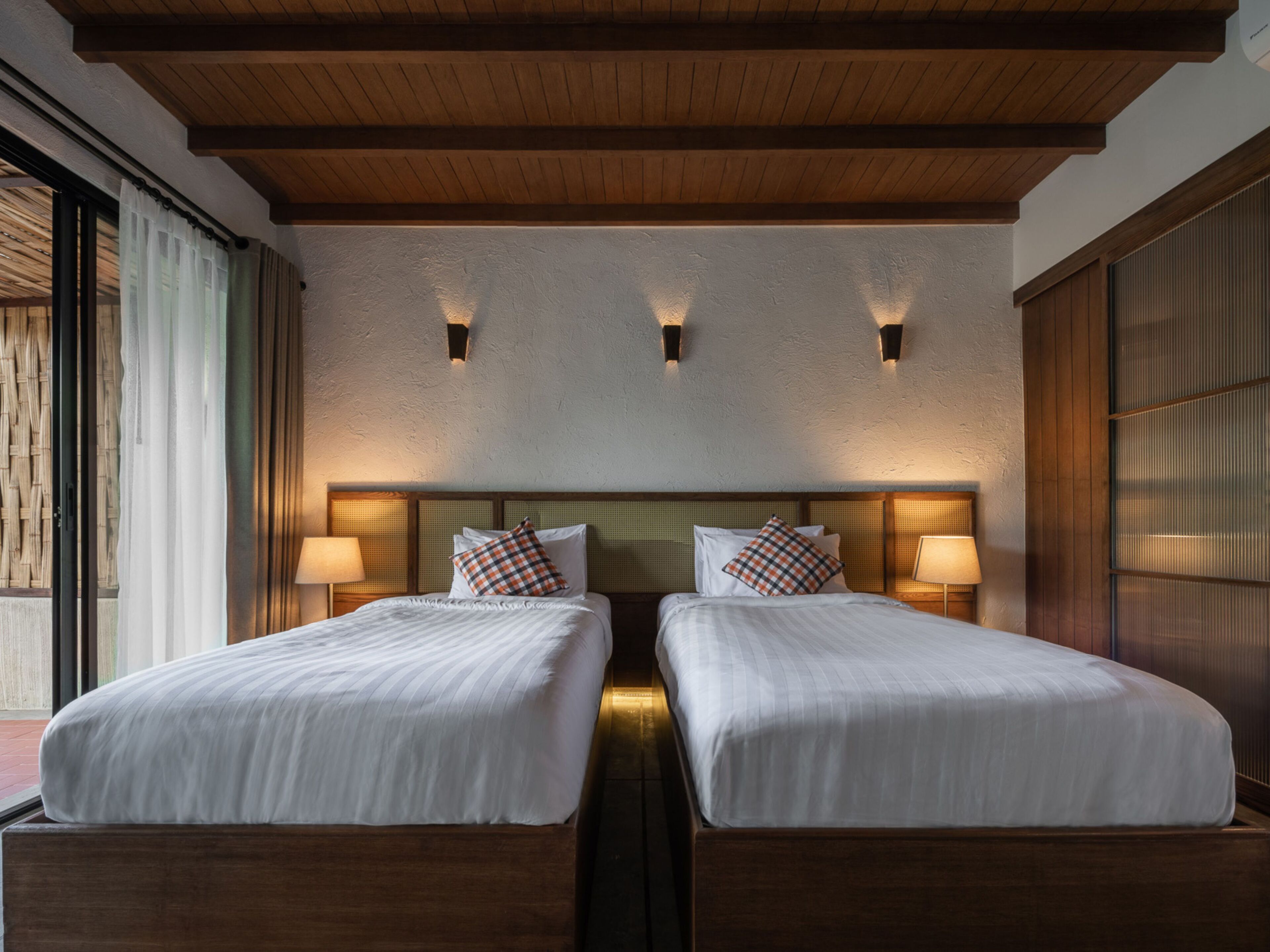 Habitación de hotel con dos camas, cabeceros de madera y lámparas de pared.