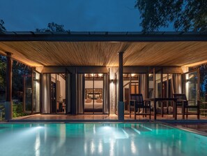 A modern house with a swimming pool, covered patio, and large glass doors leading to a bedroom.