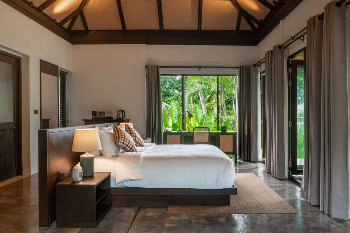 A bedroom with a large bed, bedside tables, a nightstand, and a window with curtains.