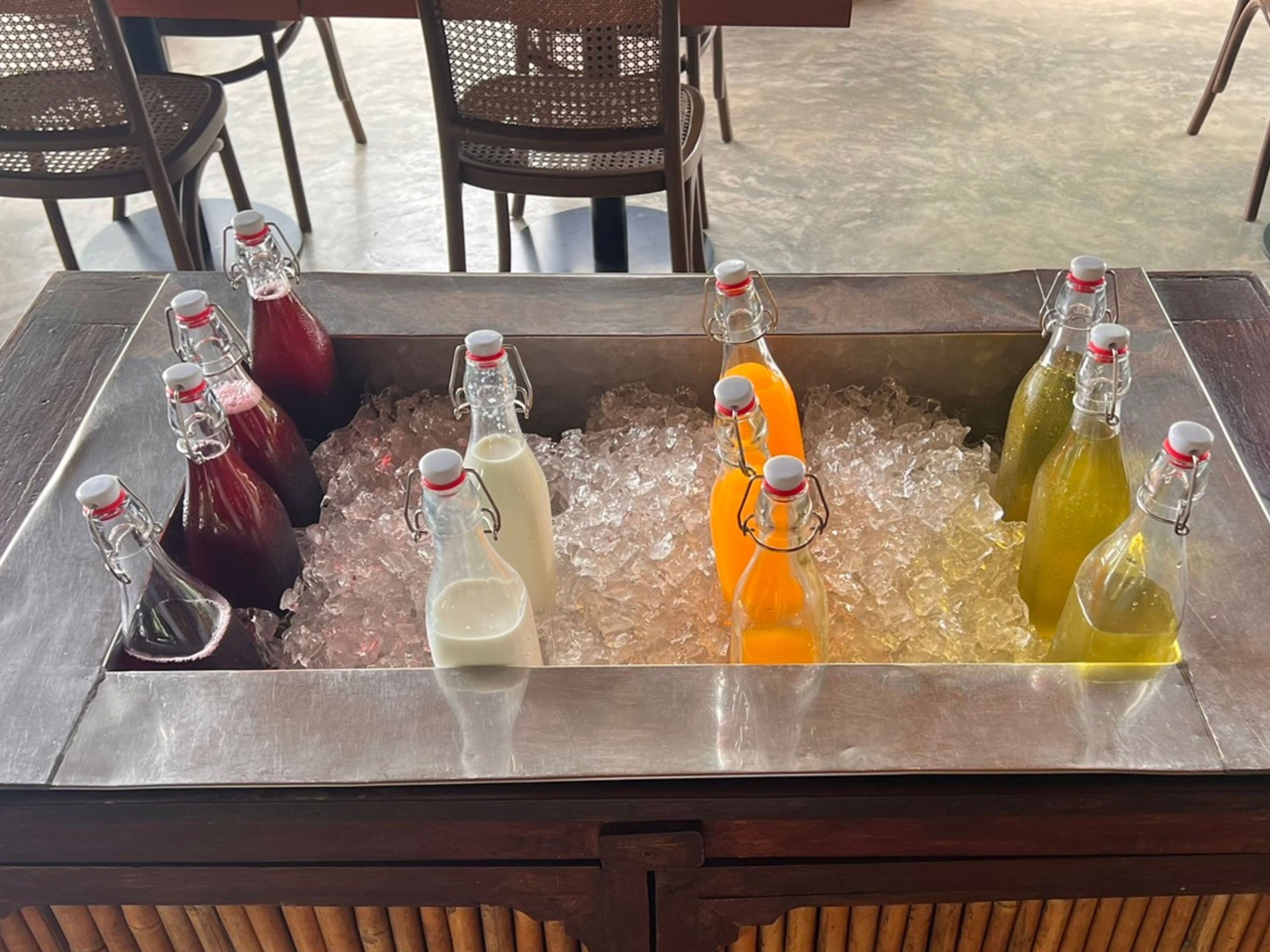 Un plateau en métal rempli de glaçons, sur lequel reposent plusieurs bouteilles en verre munies de bouchons métalliques, et qui contiennent probablement des boissons.