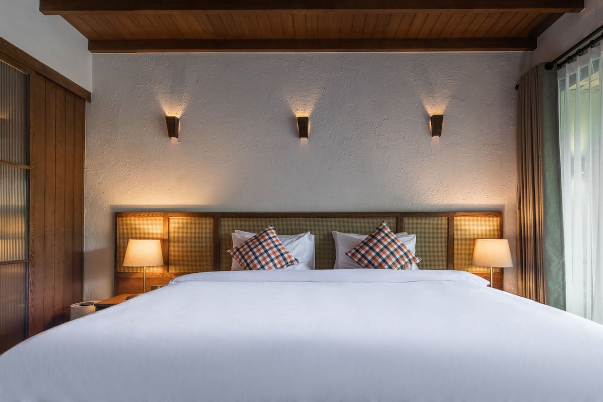 A hotel room with a large bed, two bedside lamps, and a wooden ceiling.