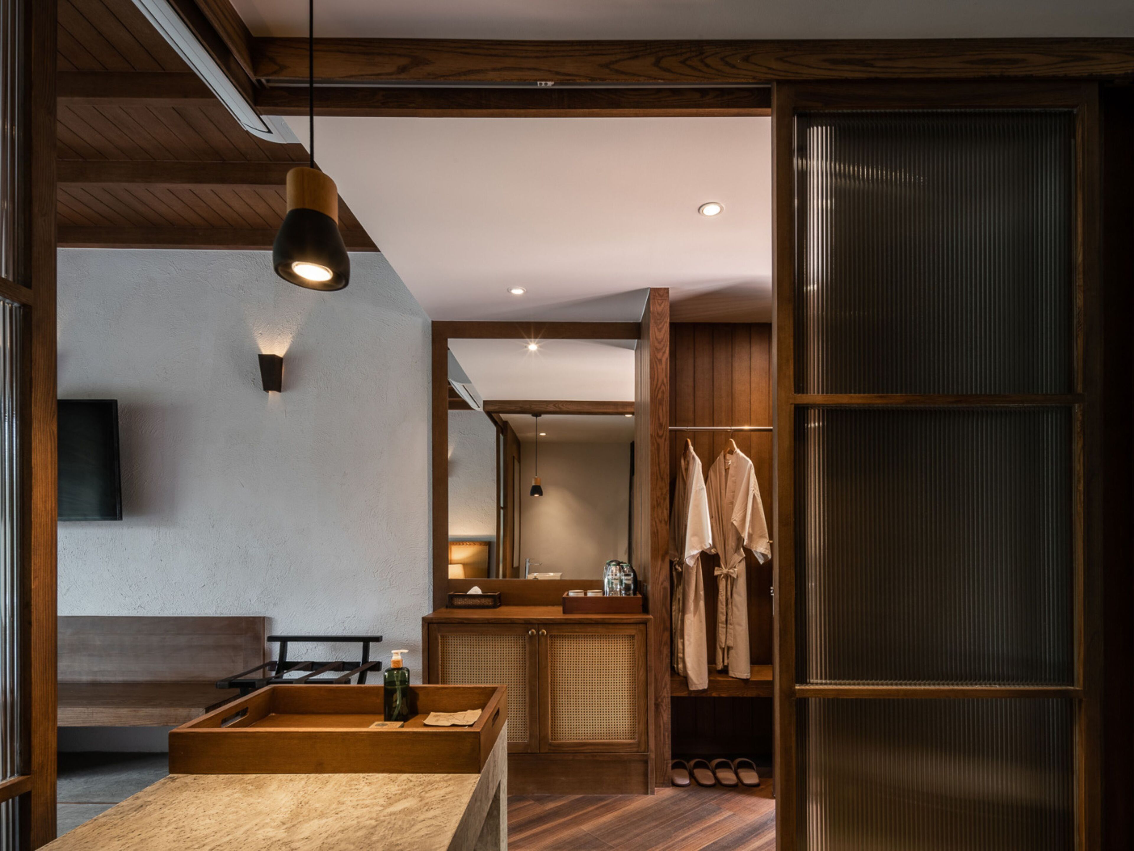 A modern bathroom with a wooden vanity, a sink, and a mirror. There is a towel rack with towels hanging, and a pair of slippers on the floor.