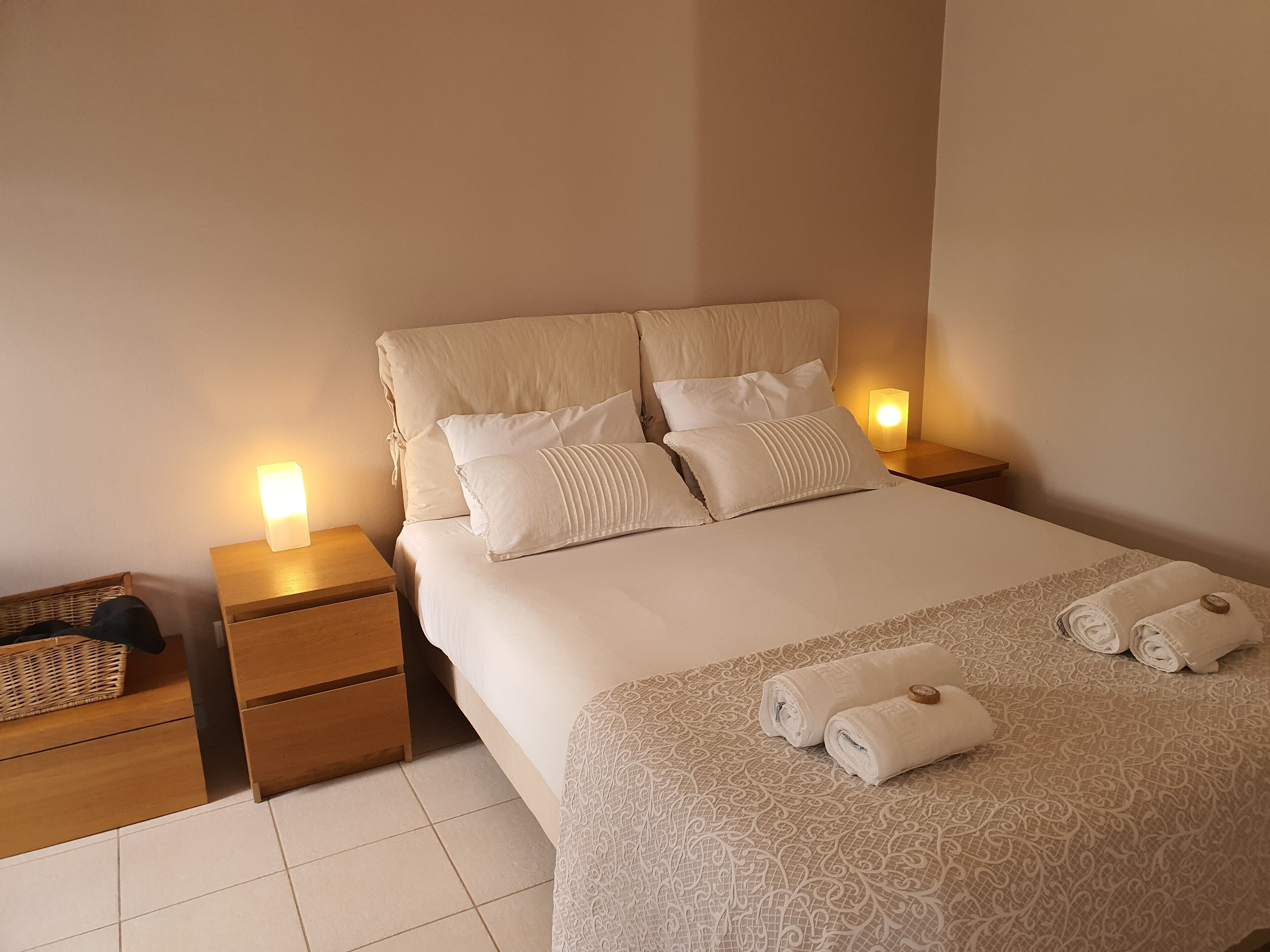 A neatly made bed with a patterned bedspread and two rolled towels on the side.