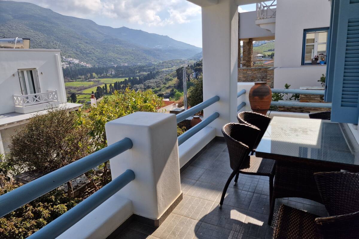 A balcony with a view of a mountainous landscape, a table, and two chairs.
