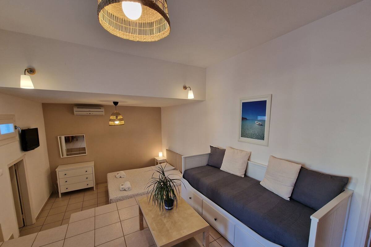 A compact living space with a sofa, a small table, a TV, and a mirror.