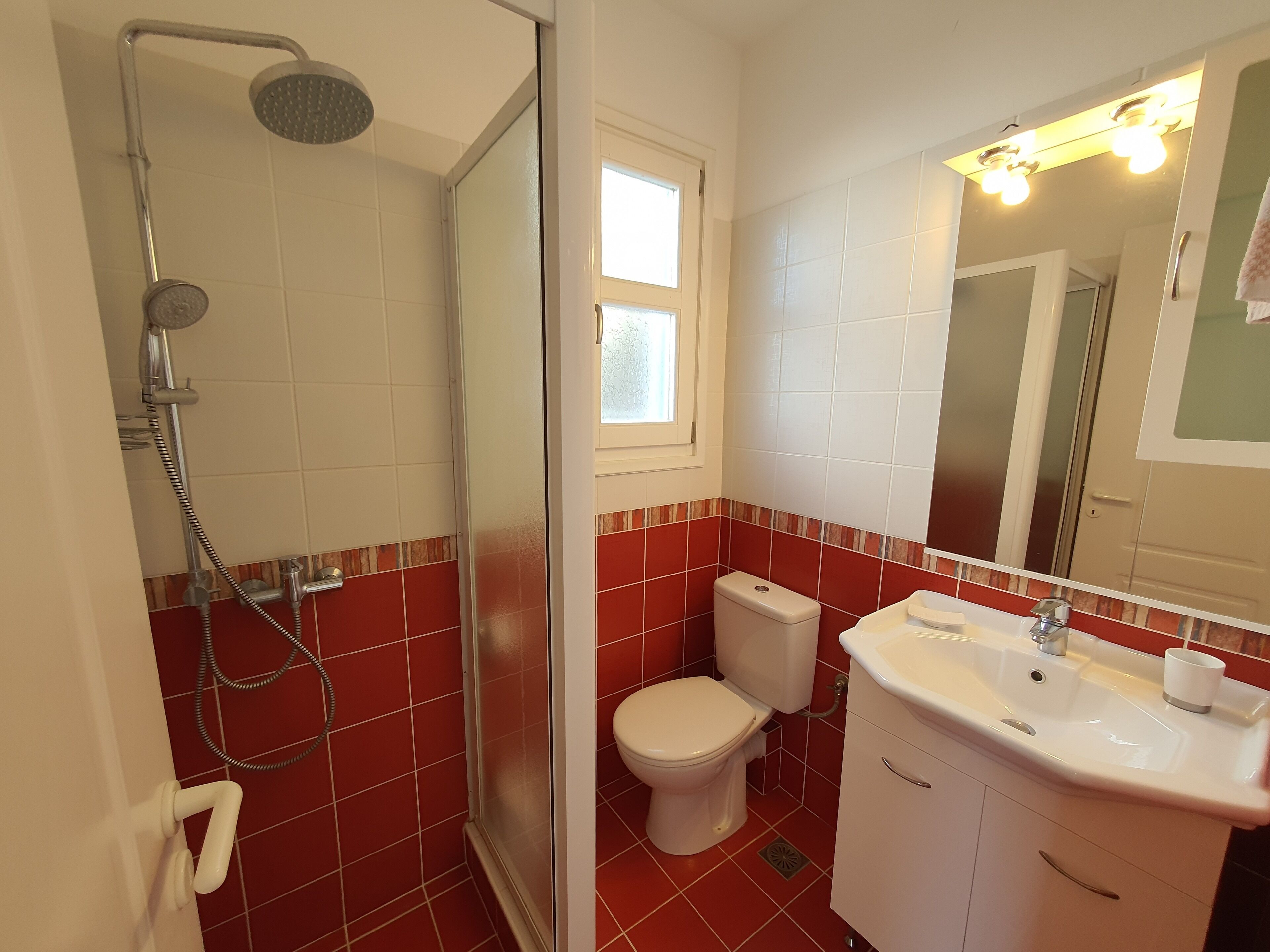 A bathroom with a shower, toilet, sink, and a window.