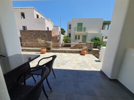 Un balcón con mesa y sillas, plantas en macetas y una pared de piedra.