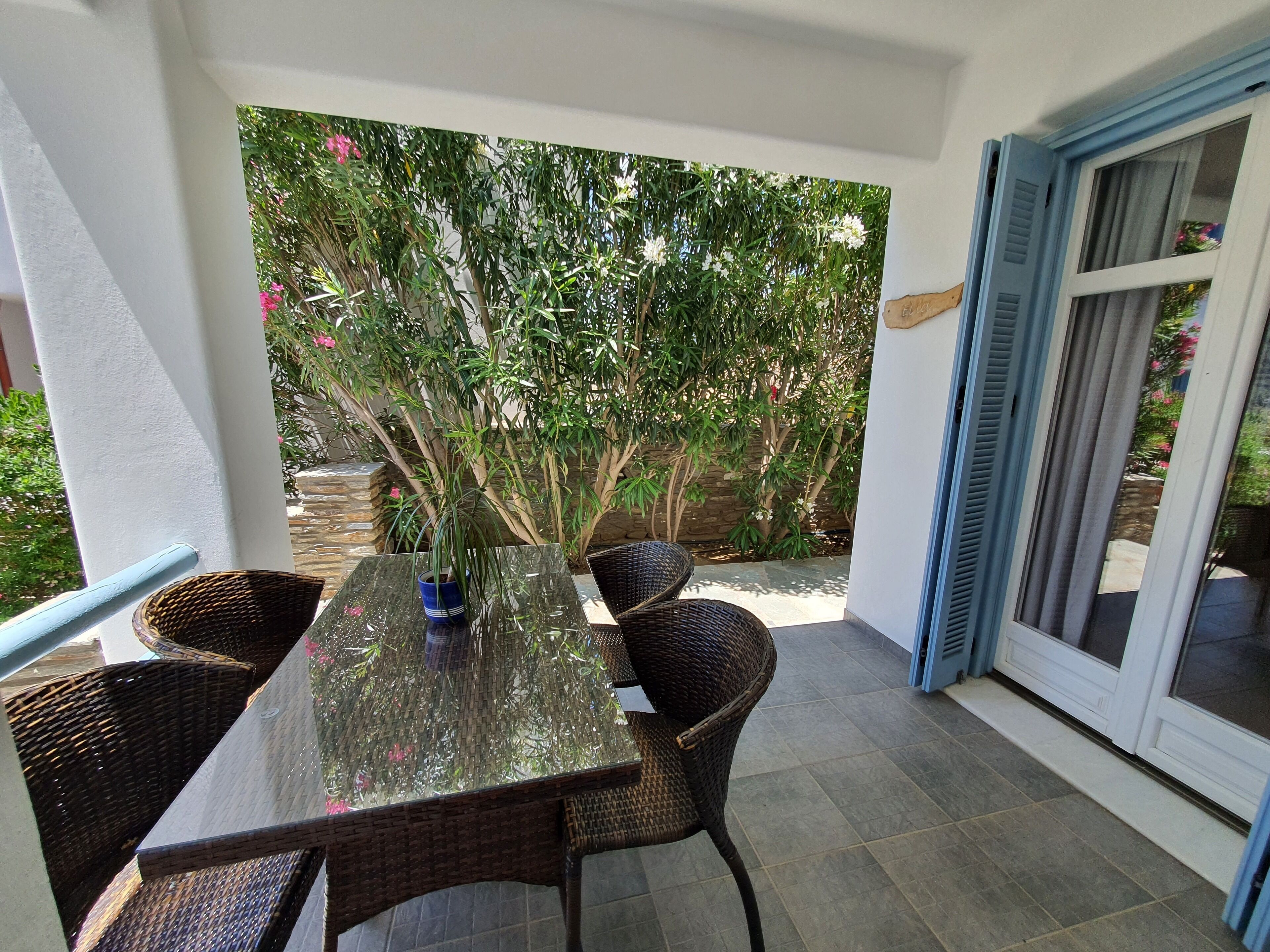 A patio with a glass-top table, wicker chairs, and a potted plant.
