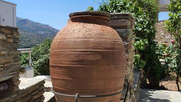 Una gran maceta de terracota en un patio de piedra, con vistas a montañas y un edificio blanco al fondo.