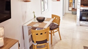 A dining area with a wooden table, two chairs, a TV, and a kitchen in the background. - A Casuccia di Mammò (Oletta)