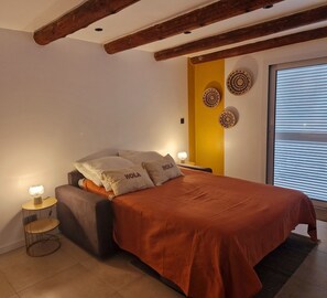 Une chambre à coucher avec un lit, deux lampes de chevet, un élément de décoration circulaire fixé au mur et une fenêtre avec des stores.