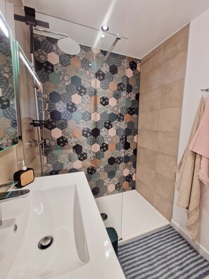 Une salle de bain moderne avec un lavabo blanc, une cabine de douche en verre et un mur recouvert de carreaux hexagonaux à motifs.