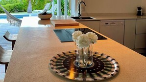 Une cuisine moderne dotée d’un îlot central, un coin repas offrant une vue sur l’extérieur et un espace piscine visible grâce à l’aménagement ouvert.