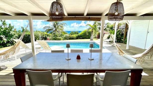 Un espace extérieur abrité, aménagé pour les repas, avec vue sur la piscine, des chaises blanches et des guirlandes lumineuses.