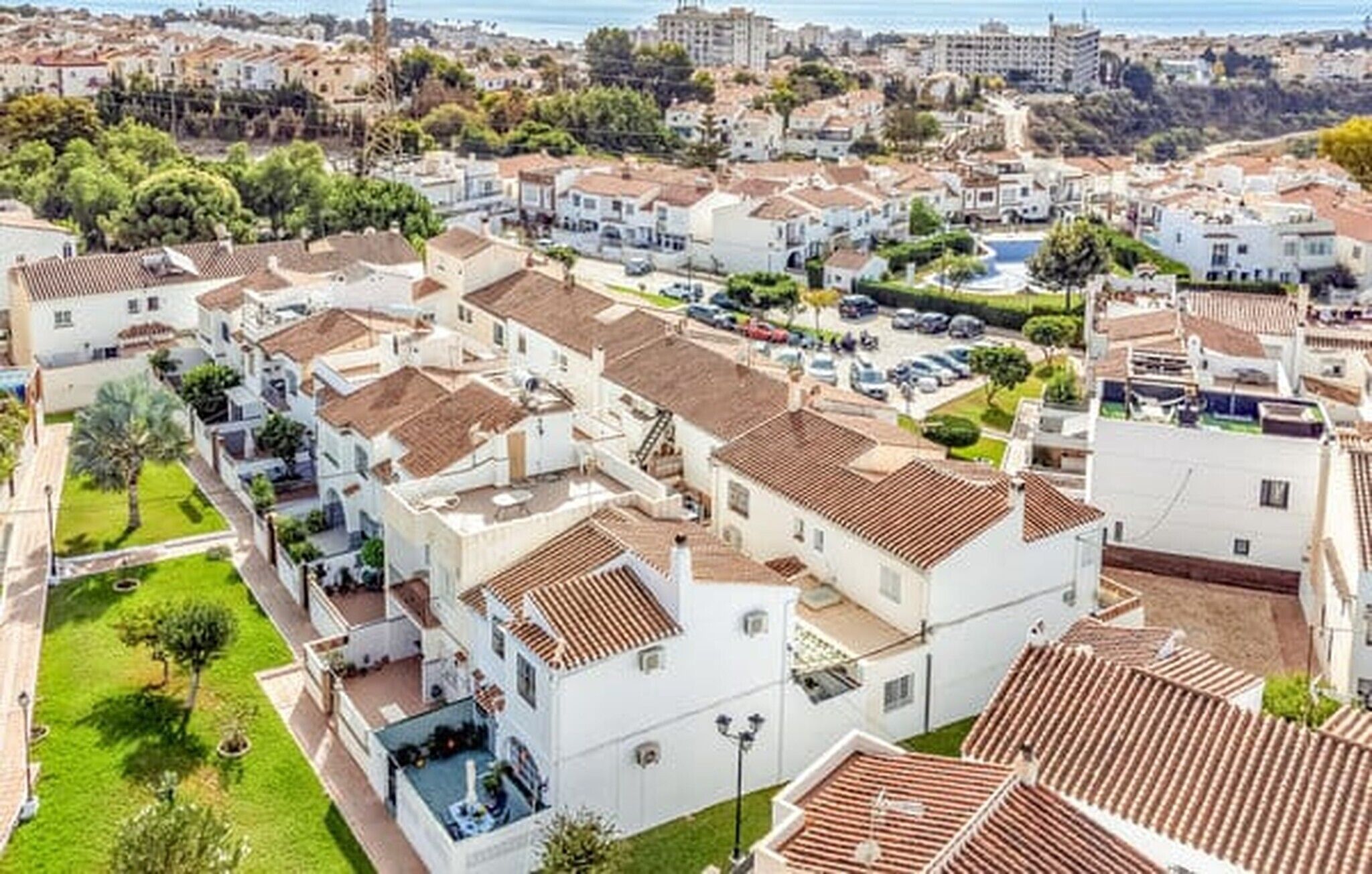 A residential area with white houses, terracotta roofs, and a view of the sea.