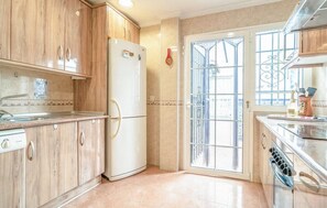 A kitchen with wooden cabinets, a white refrigerator, a sink, and a window with metal bars.