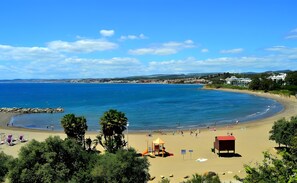 A beach with a playground, a lifeguard tower, and a view of the sea and distant buildings.