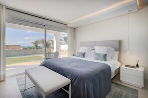 A modern bedroom with a large bed, a bench, a nightstand, and a view of the outdoors.