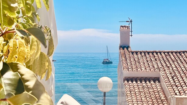 Une terrasse avec vue sur la mer, un voilier et une chaise blanche.