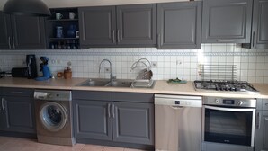 A kitchen with grey cabinets, a washing machine, a dishwasher, a stove, and a coffee maker. - Holiday Home 'Picotelle' with Private Terrace, Private Garden and Wi-Fi (Le Château d'Oléron)