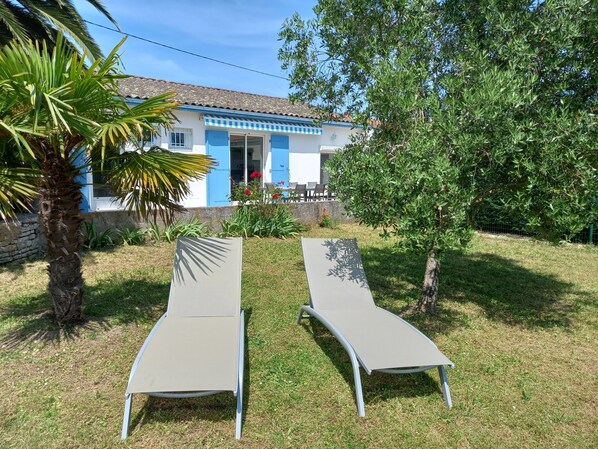 Il s’agit d’une propriété comprenant un bâtiment aux couleurs bleu et blanc, deux fauteuils de jardin, un palmier et un jardin.