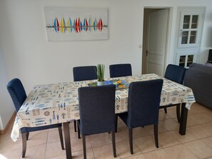 Un coin repas avec une table recouverte d’une nappe à motifs, entourée de chaises, et une œuvre d’art accrochée au mur au-dessus.