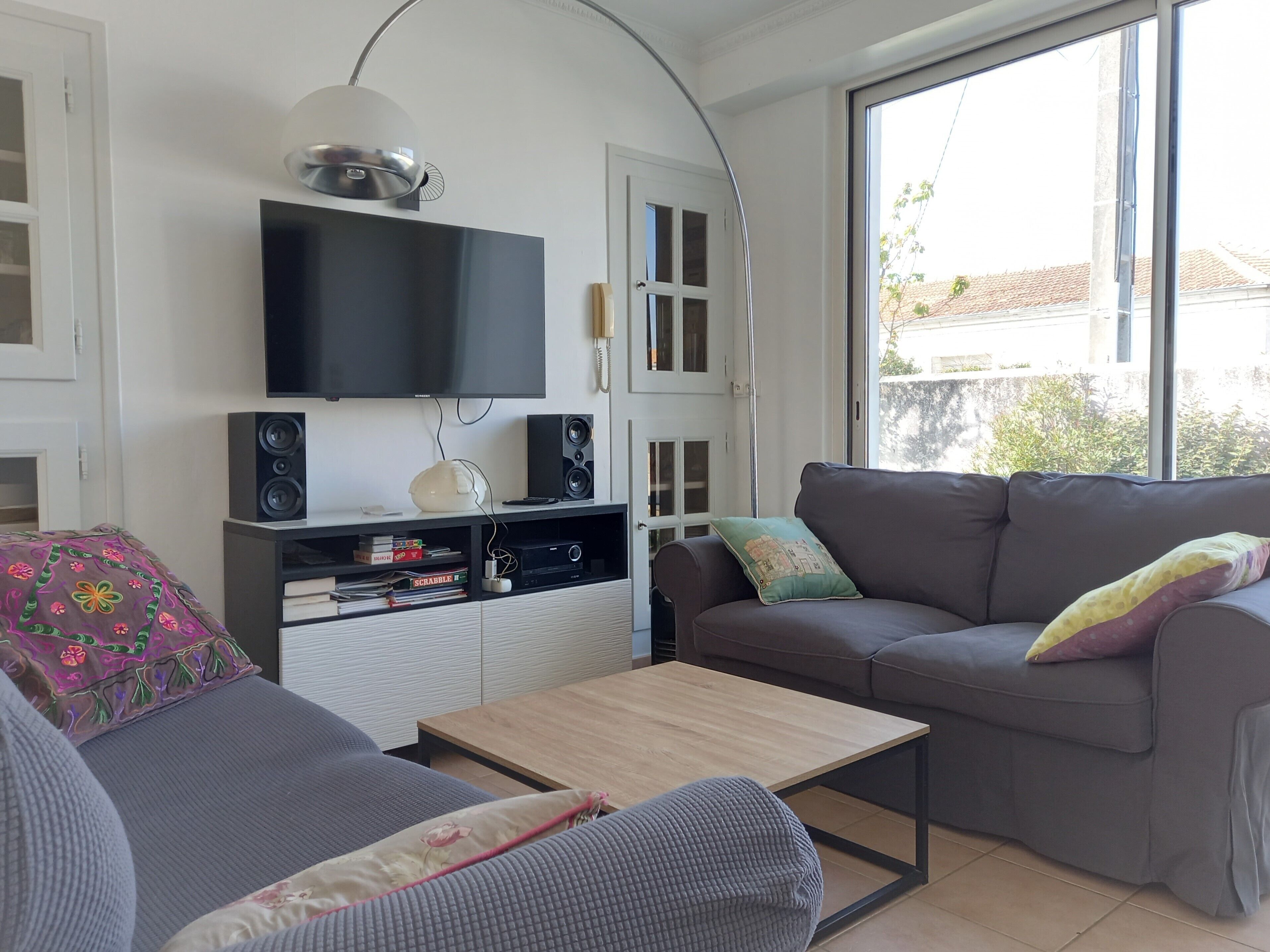 A living room with a flat-screen TV, speakers, a sofa, a coffee table, and a large window.