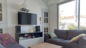 A living room with a flat-screen TV, speakers, a sofa, a coffee table, and a large window. - Holiday Home 'Picotelle' with Private Terrace, Private Garden and Wi-Fi (Le Château d'Oléron)
